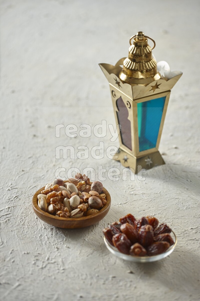A golden lantern with different drinks, dates, nuts, prayer beads and quran on textured white background