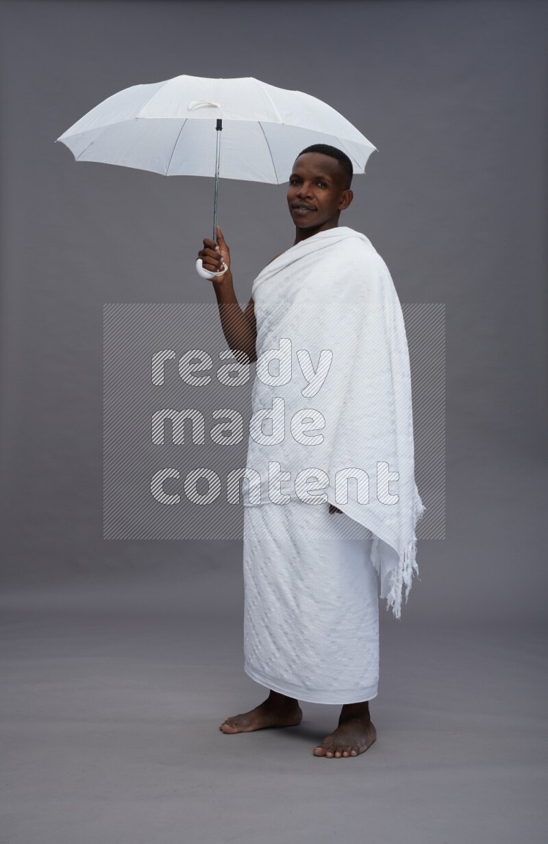A man wearing Ehram Standing holding umbrella on gray background