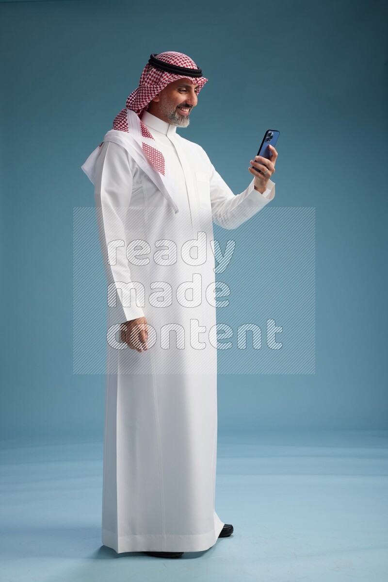 Saudi man wearing thob and shomagh texting on blue background