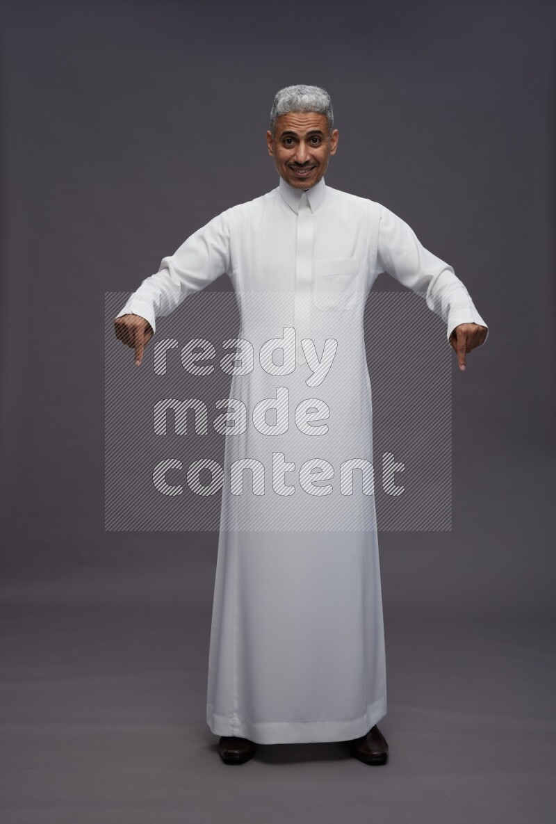 Saudi man wearing thob standing interacting with the camera on gray background