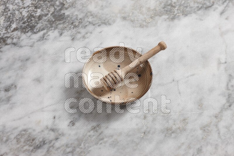 Multicolored pottery bowl with wooden honey dipper in it on grey marble background