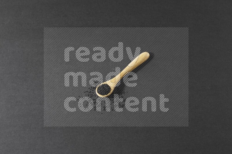 ملعقة خشبية ممتلئة بحبة البركة مع بعض الحبوب منتشرة بجانبها على أرضية سوداء