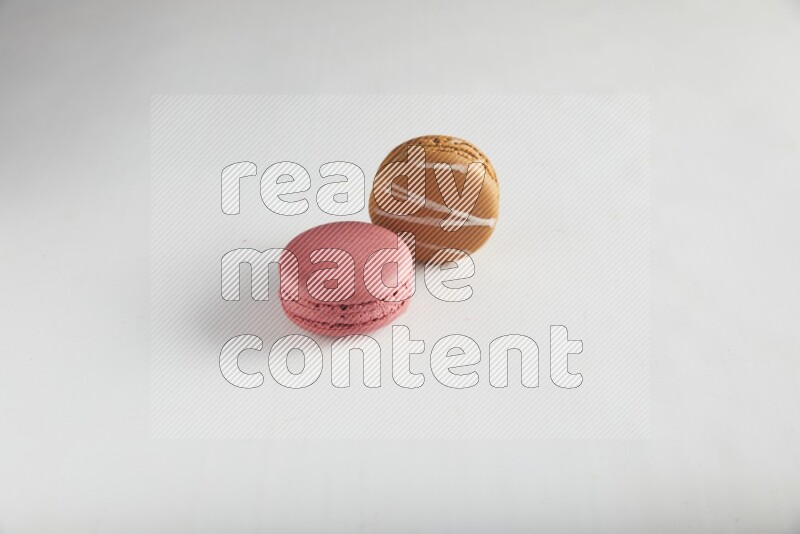 45º Shot of of two assorted Brown Irish Cream, and Pink Raspberry macarons on white background