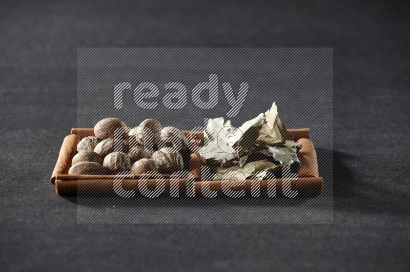 2 squares of cinnamon sticks full of nutmegs and bay laurel leaves on black flooring