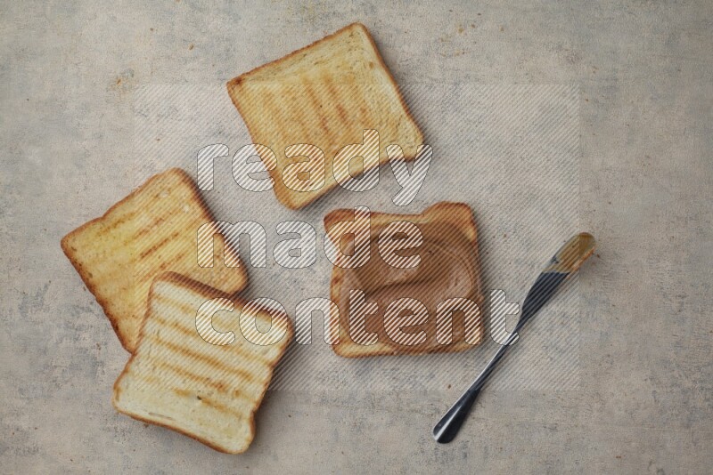 Creamy peanut butter on a toasted white toast and toasted white toast slices on a light blue textured background