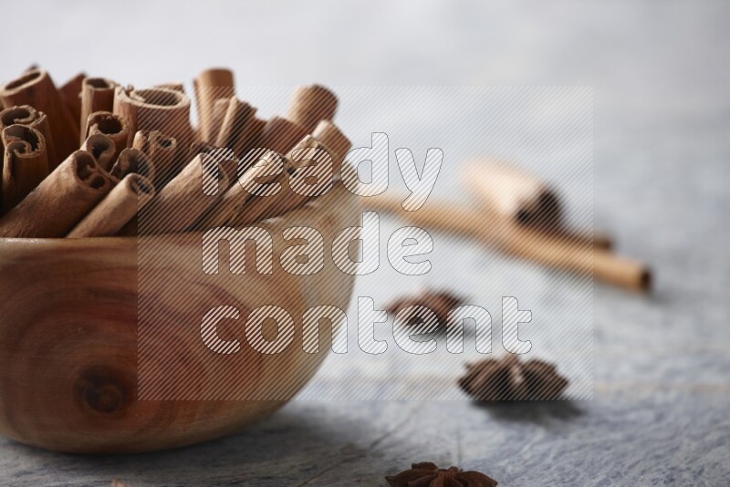 wooden bowl full of cinnamon sticks surrounded by star anis on marble background in different angles