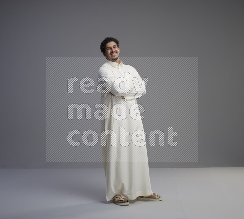A Saudi man standing wearing thob interacting with the camera on gray background