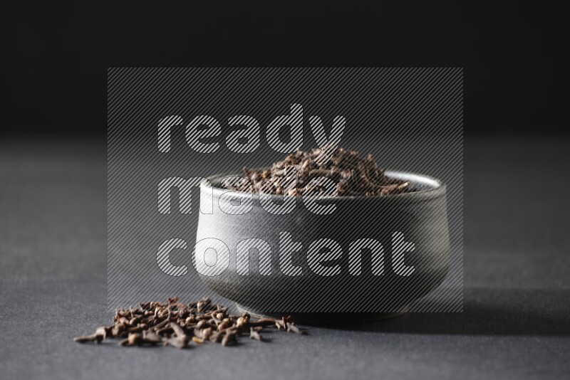 A black pottery bowl full of cloves on a black flooring