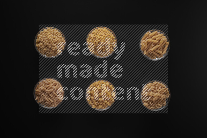 Different pasta types in 6 glass bowls on black background