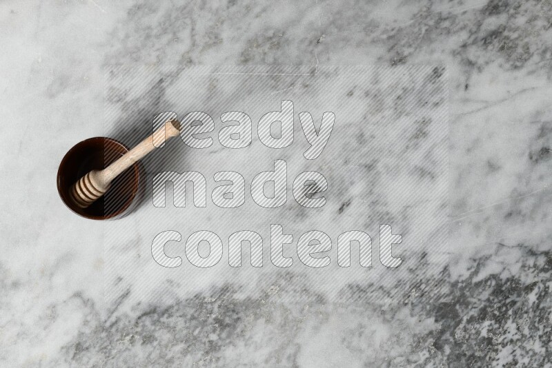 Brown pottery bowl with wooden honey dipper in it on grey marble background