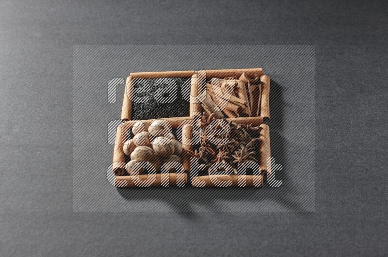 4 squares of cinnamon sticks full of black seeds, cinnamon, star anise and nutmegs on black flooring