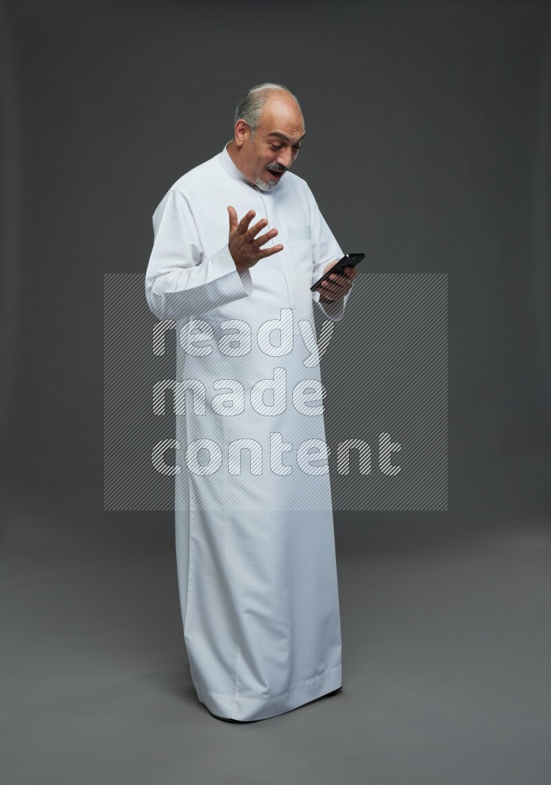 Saudi man without shomag Standing texting on phone on gray background