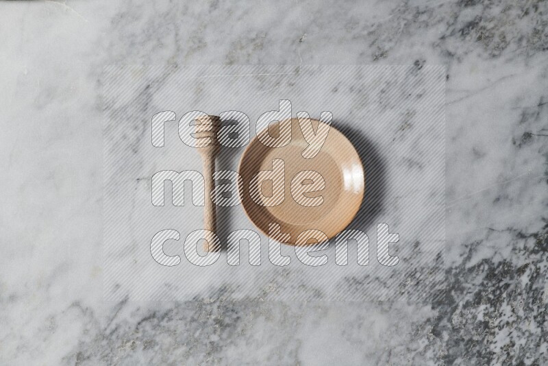 Beige pottery plate with wooden honey dipper on the side on grey marble background