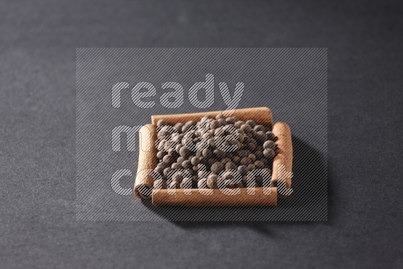 A single square of cinnamon sticks full of allspice on black flooring