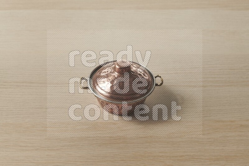 A small copper pot on light wooden background
