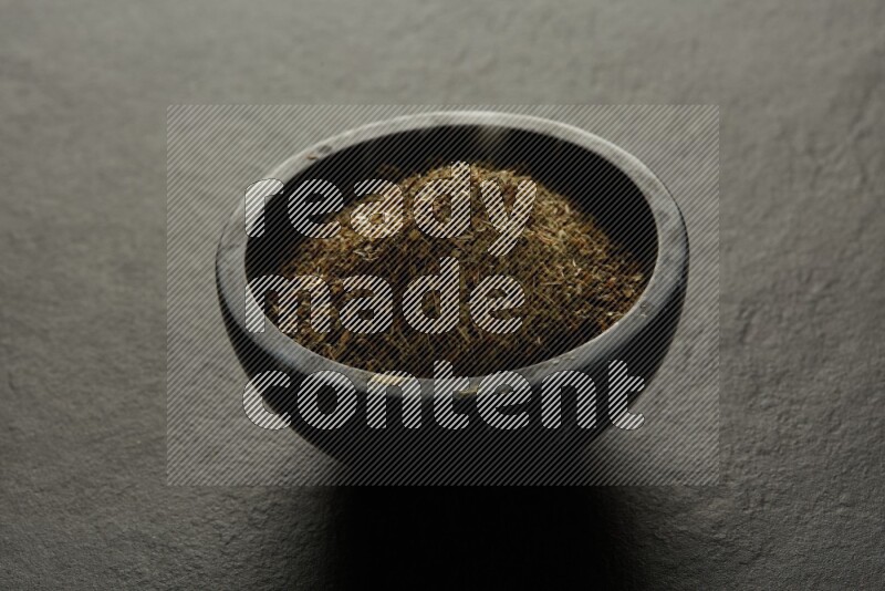 black pottery round sauce bowl filled with herbs on grey textured countertop