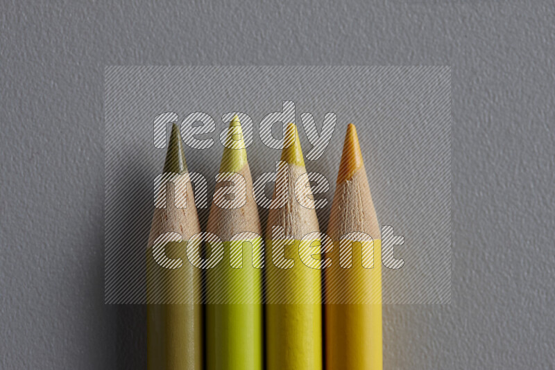 A collection of sharpened colored pencils arranged showcasing a gradient of yellow hues on grey background