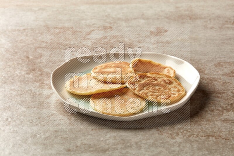 Five stacked plain mini pancakes in a bicolor plate on beige background