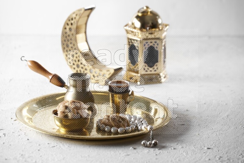 Dried figs in a metal bowl with coffee and prayer beads on a tray beside lanterns in a light setup