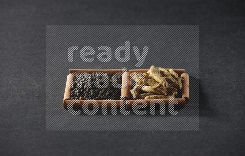 2 squares of cinnamon sticks full of black peppers and turmeric fingers on black flooring