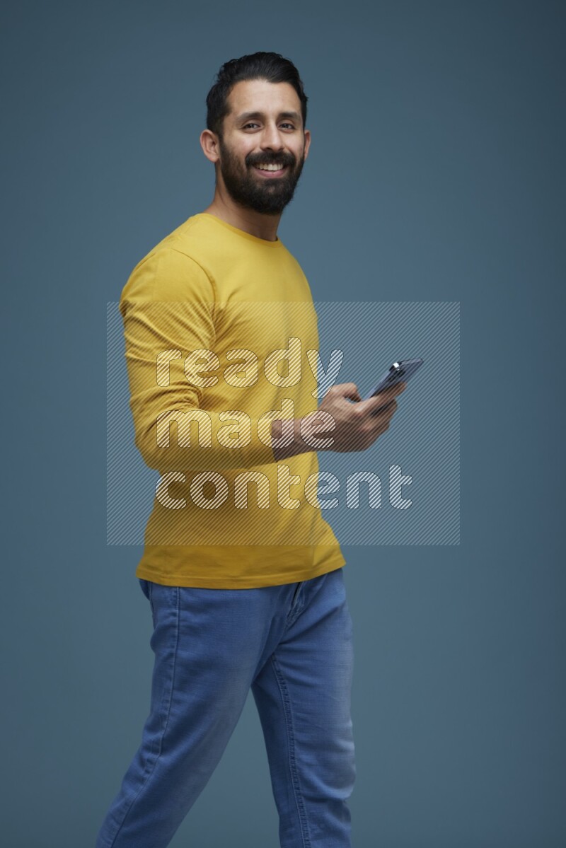 Man posing with a phone in a blue background wearing a yellow shirt
