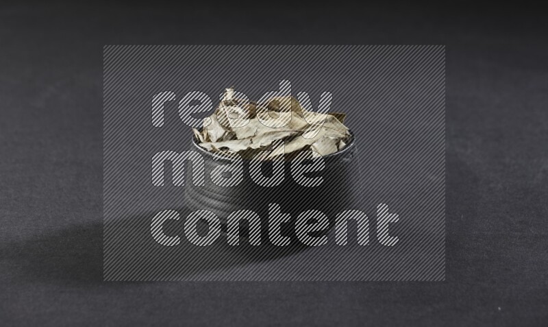 وعاء فخاري أسود ممتلئ بأوراق الغار المجففة على أرضية سوداء