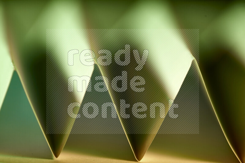 A close-up abstract image showing sharp geometric paper folds in green gradients and warm tones