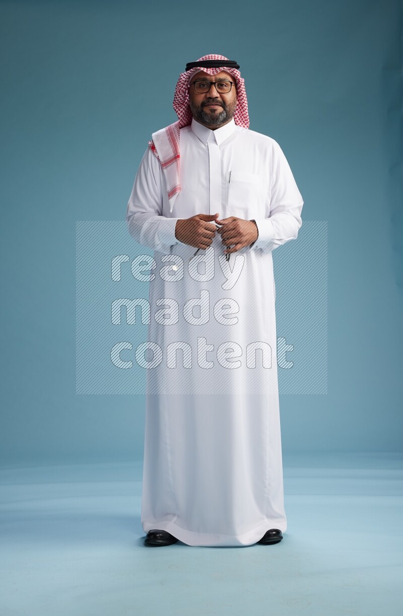 Saudi Man with shimag Standing Interacting with the camera on blue background