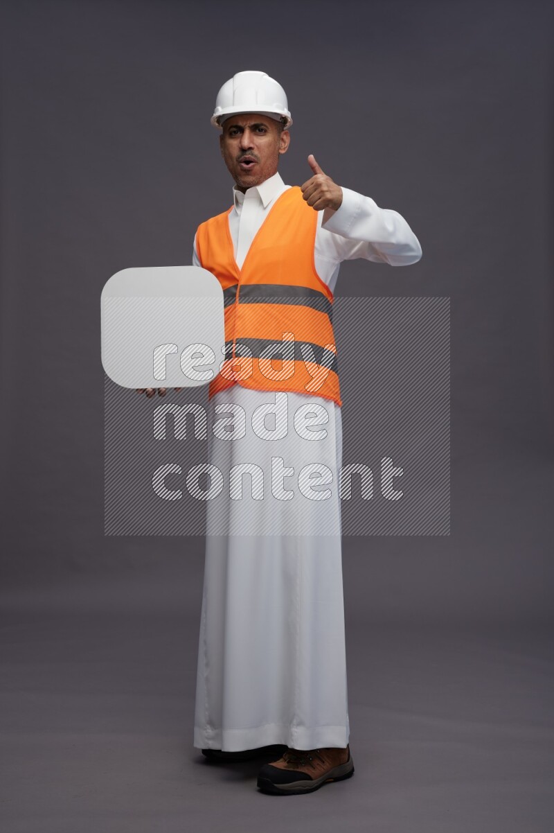 Saudi man wearing thob with engineer vest standing holding social media sign on gray background
