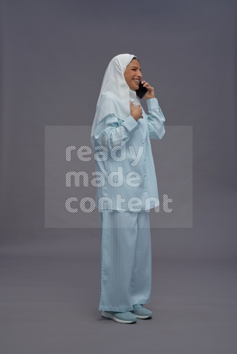 Saudi woman wearing hijab clothes standing talking on phone on gray background