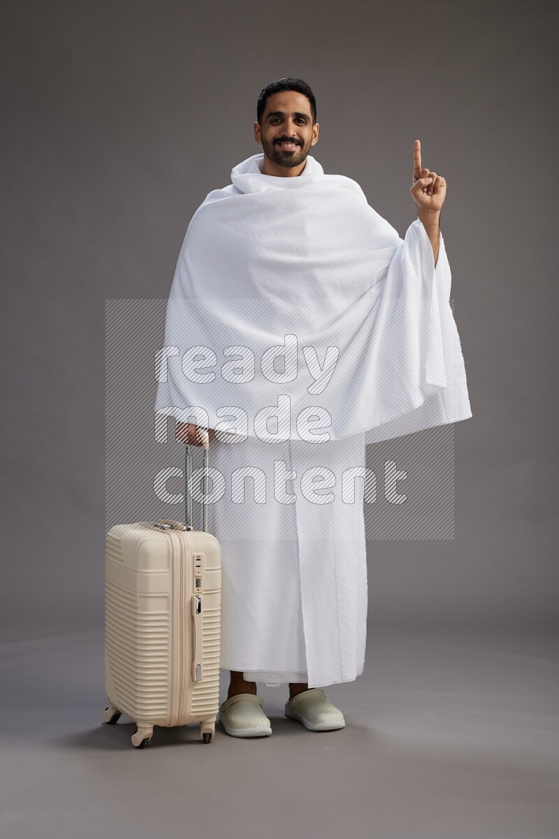A man wearing Ehram Standing holding traveling bag on gray background