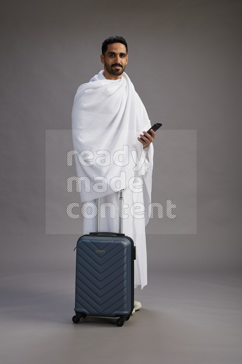 A man wearing Ehram Standing holding traveling bag on gray background