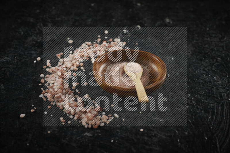 A pottery plate full of fine salt with bunch of coarse salt beside it on black background