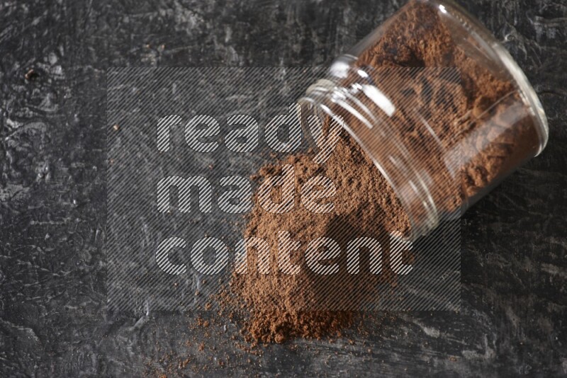A flipped glass jar full of cloves powder on a textured black flooring