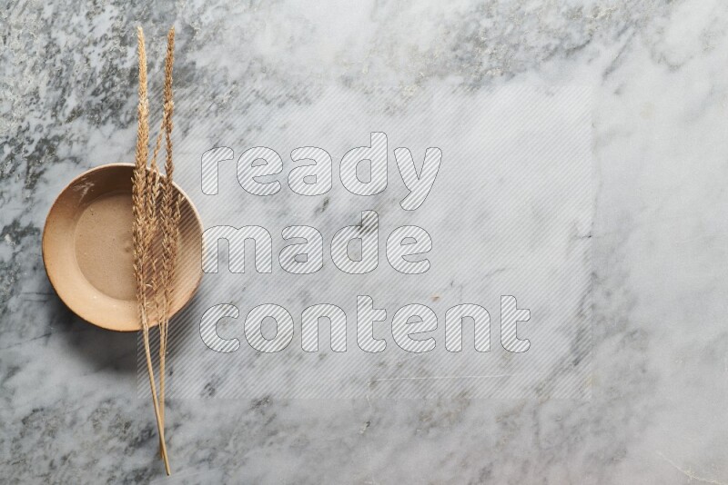 Wheat stalks on beige pottery plate on grey marble background