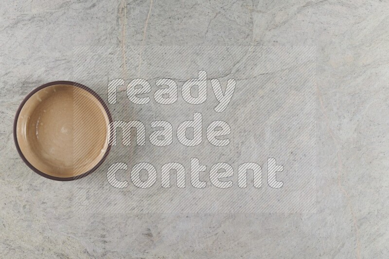 A beige pottery oven bowl on grey marble background