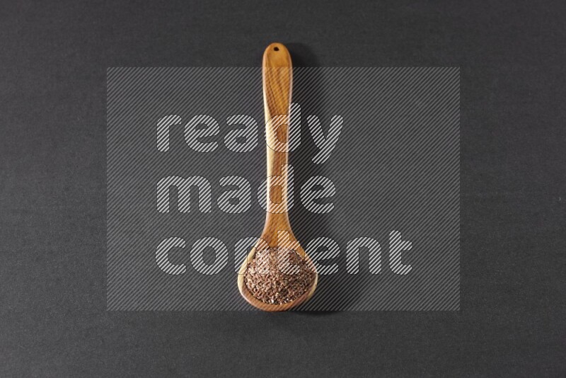 A wooden ladle full of flaxseeds on a black flooring