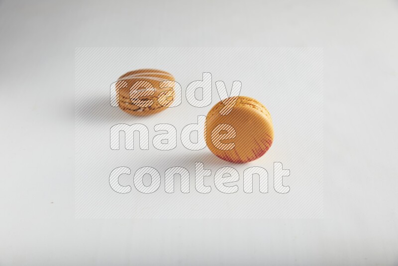 45º Shot of of two assorted Brown Irish Cream, and Orange Exotic macarons on white background