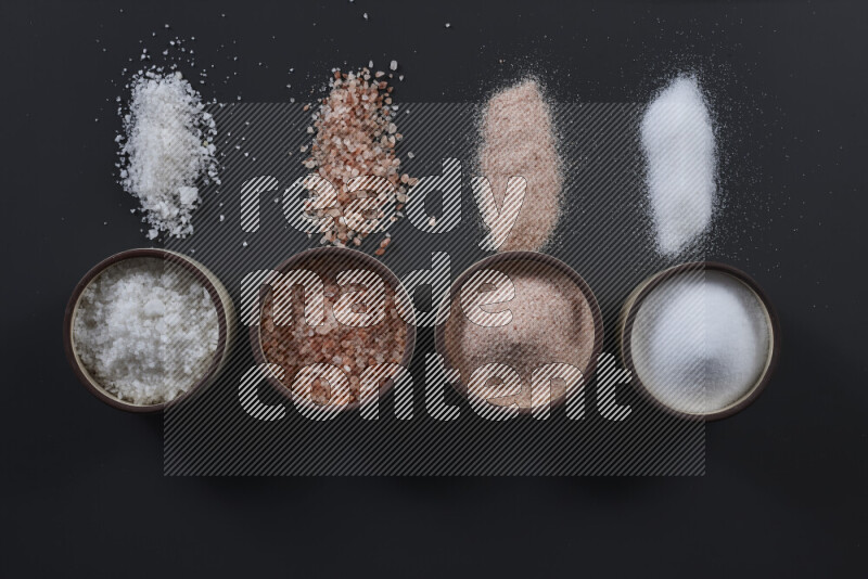4 pottery bowls filled with himalayan salt and white salt on black background