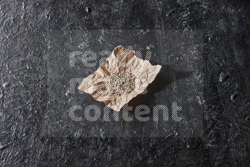 حبوب الفلفل الأبيض في قطعة من الورق على أرضية سوداء