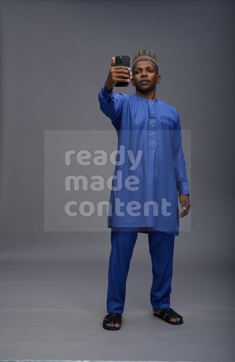Man wearing Nigerian outfit standing taking selfie on gray background