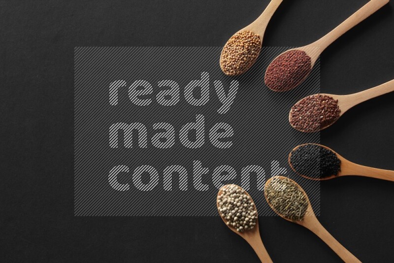 wooden spoons filled with white peppers, mustard seeds, black seeds, garden cress, cumin and flax on black flooring