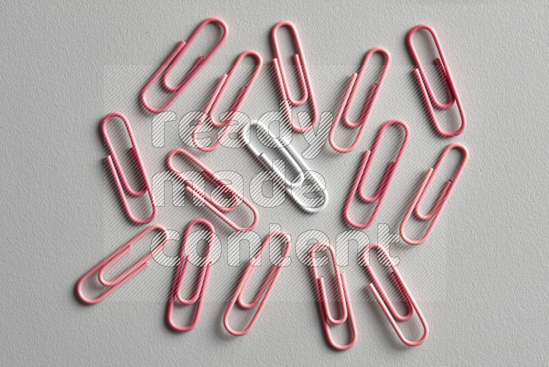A bunch of pink paper clips with a different colored paper clip in the center on grey background