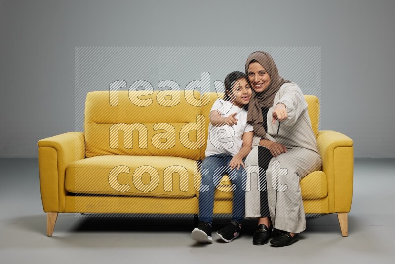 A girl with her mother sitting and interacting with the camera on gray background