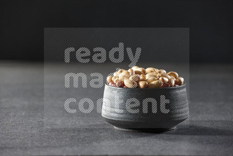 A black pottery bowl full of peeled peanuts on a black background in different angles