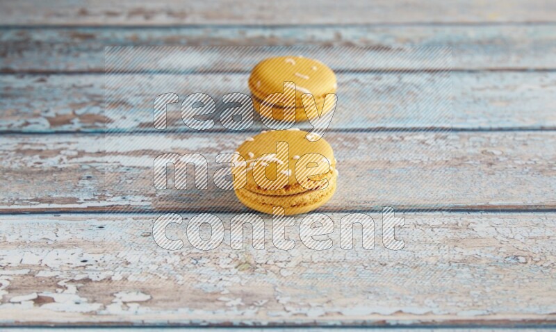 45º Shot of two Yellow Piña Colada macarons on light blue wooden background