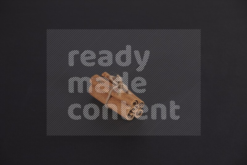 4 Cinnamon sticks stacked and bounded on black flooring