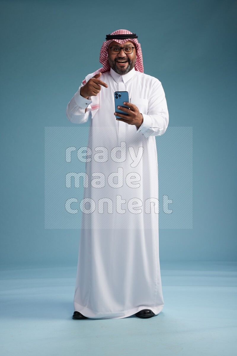 Saudi Man with shimag Standing texting on phone on blue background