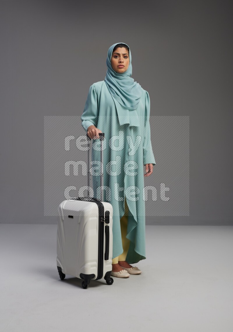 Saudi Woman wearing Abaya standing holding Travel bag on Gray background