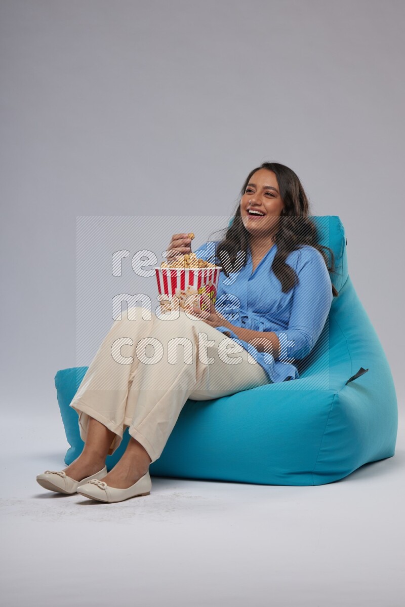 A woman sitting on a blue beanbag and eating popcorn